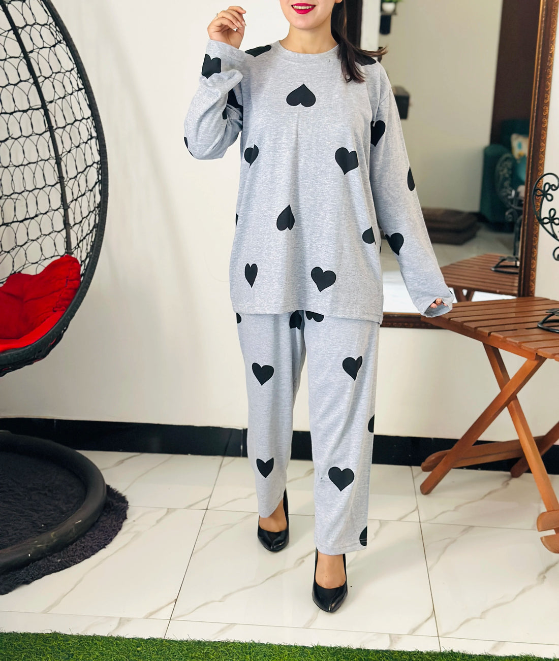 Person wearing a gray outfit with black heart patterns in a room with a chair and table.