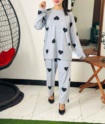 Person wearing a gray outfit with black heart patterns in a room with a chair and table.