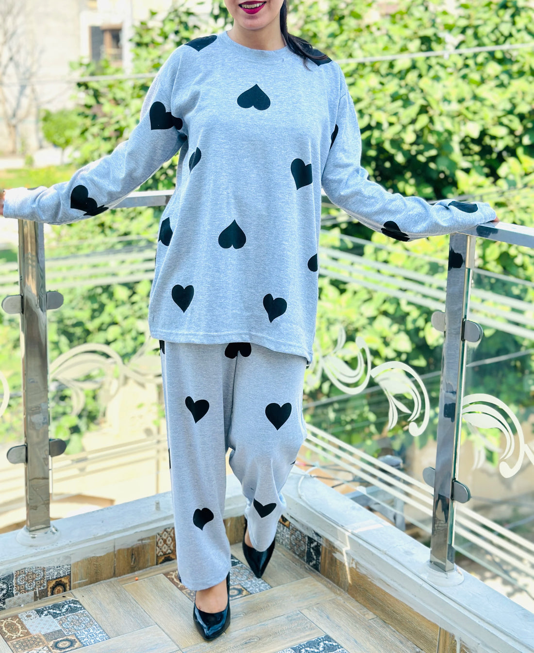 Person wearing a gray outfit with black heart patterns in a room with a chair and table.